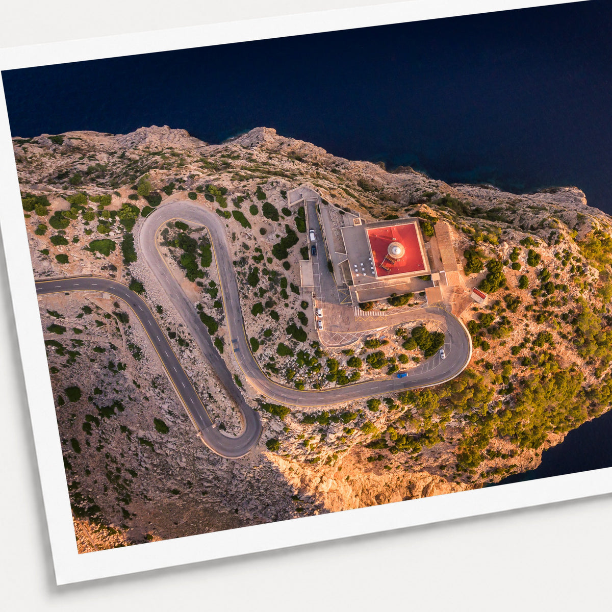 A photographic print of Cap De Formentor Lighthouse from above, shown with a white border and angled presentation on a light background.