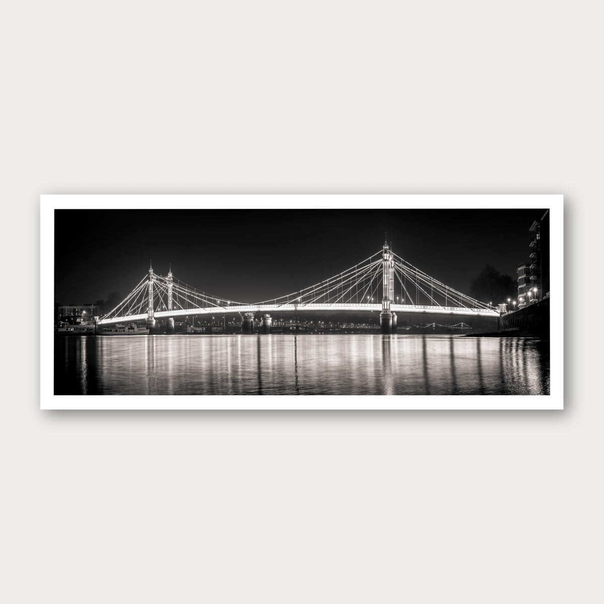A photographic print of Albert Bridge by Night, framed with a white border and shown against a light gray background.