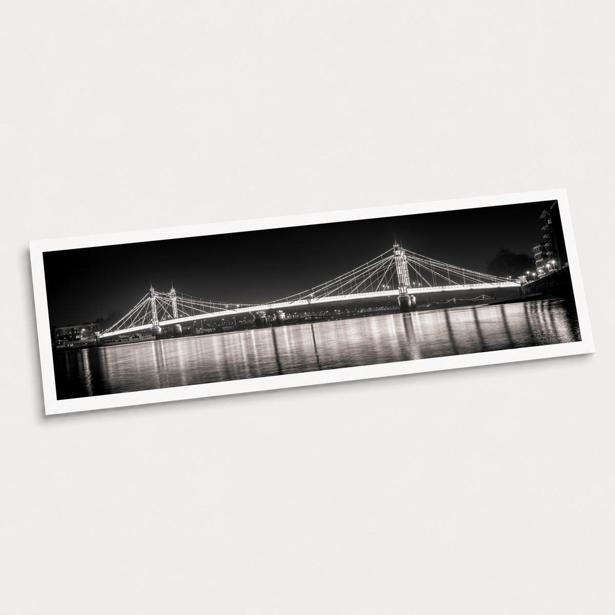 A photographic art print of Albert Bridge by Night, displayed at an angle on a light gray background.