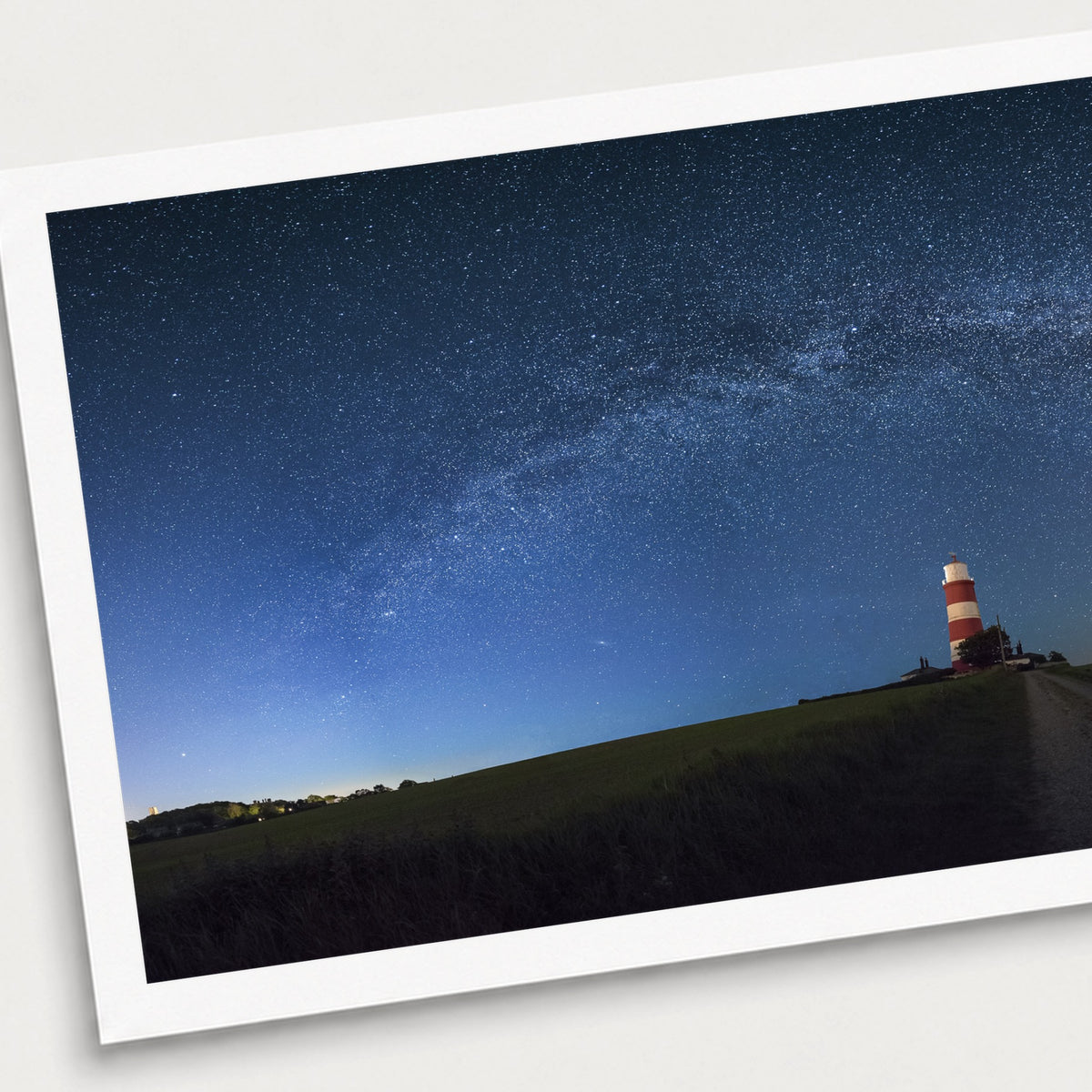 A photographic print of Happisburgh Lighthouse Milky Way, shown with a white border and angled presentation on a light background.