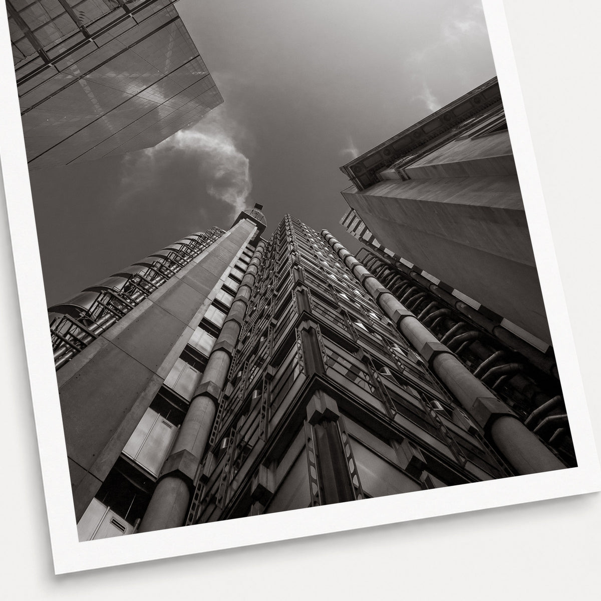 A black and white photographic print of Looking up at Lloyds, shown with a white border and angled presentation on a light background.